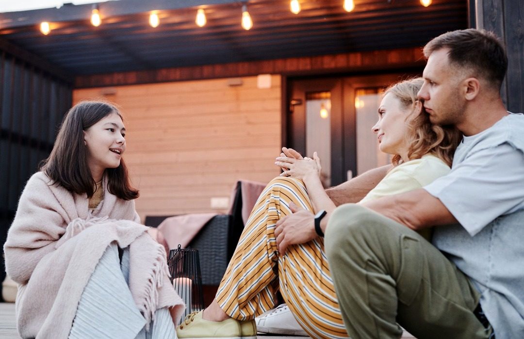 A teenage girl chatting and smiling with her parents outside on a summer evening